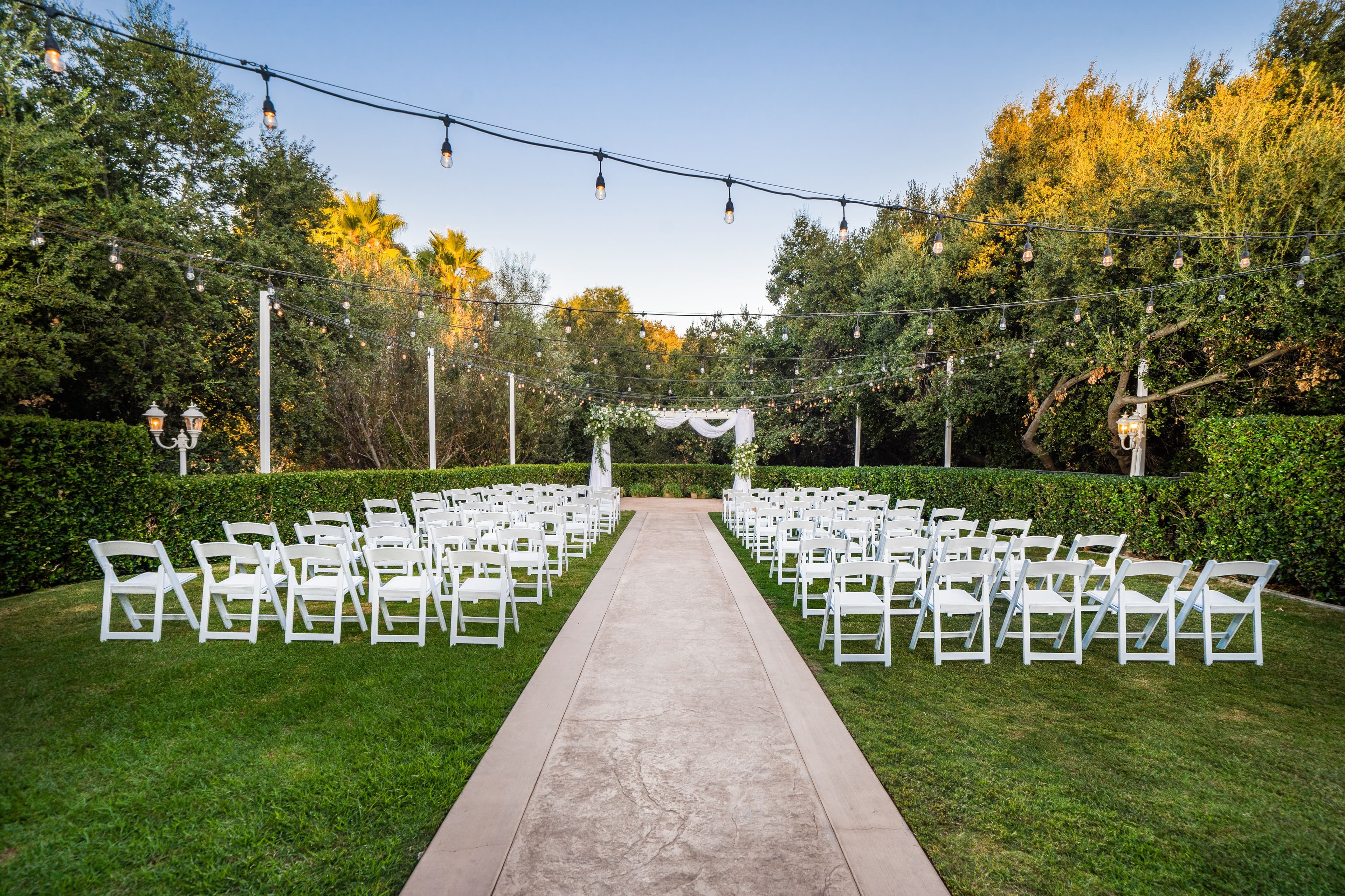 Ceremony lawn at Sierra La Verne by Wedgewood Weddings filled with white folding chairs and string lights above.
